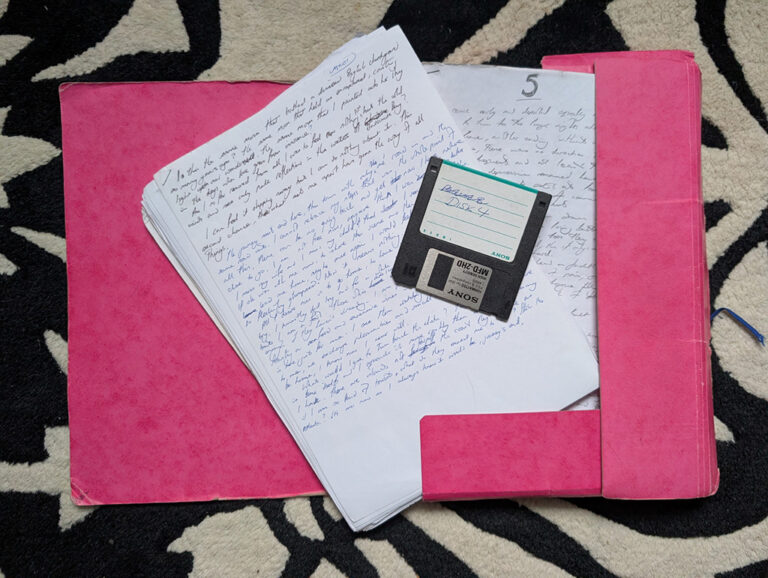 Handwritten pages of the original manuscript of The Reader and the Writer in a pink folder, with a floppy disk labelled Backup B Disk 4